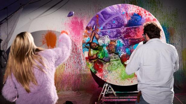 Heidi Klum bewirft in der Sendung „Germany’s Next Topmodel“ einen Kandidaten mit Farbe, während ein Fotograf die Szene festhält.