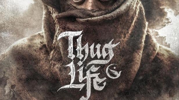 Ein Mann mit einem Tuch vor dem Gesicht, im Hintergrund eine Gruppe von Gestalten und der Schriftzug „Thug Life“.