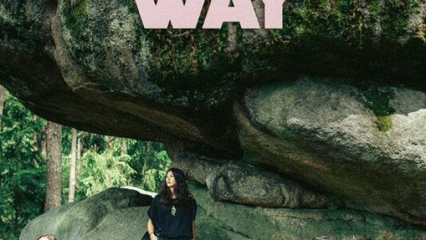 Drei Personen sitzen unter einem großen Felsen im Wald.