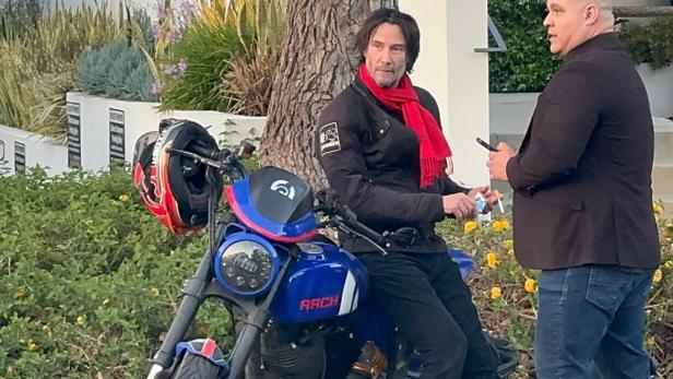 Keanu Reeves sitzt auf einem Arch Motorrad und spricht mit einem Mann.