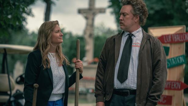 Eine Frau und ein Mann stehen vor einem Wegweiser mit dem Schriftzug „Luftballon Station“.