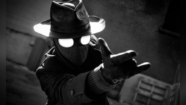 Ein Spider-Man Noir-Cosplayer in einem Hut und Mantel streckt seine Hand aus.