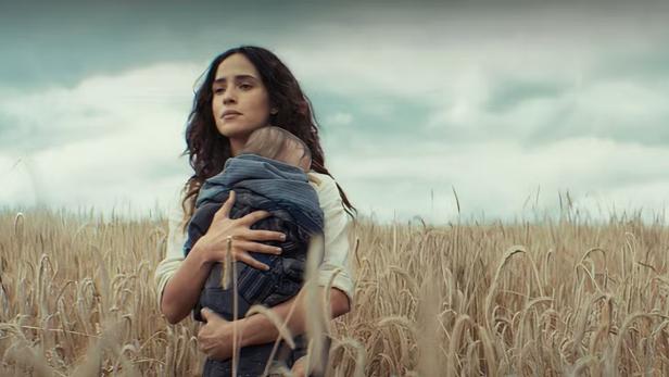 Eine Frau trägt ein Baby in einem Feld mit hohem Gras.