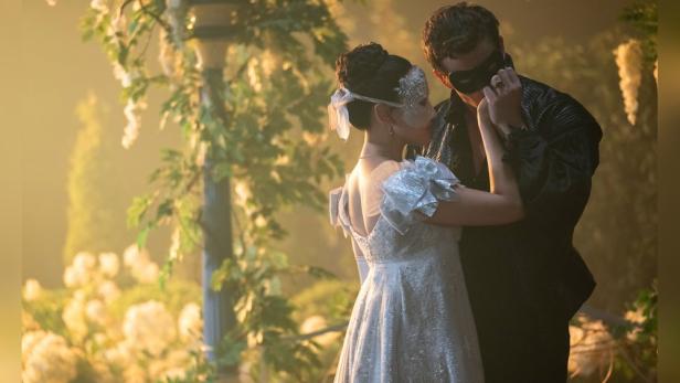 Ein Paar, gekleidet für einen Maskenball, tanzt; vermutlich Luke Thompson und Yerin Ha aus „Bridgerton“.