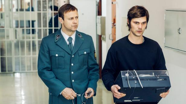 Ein Gefängniswärter und ein Häftling mit einem Plattenspieler in einem Gefängnisflur.