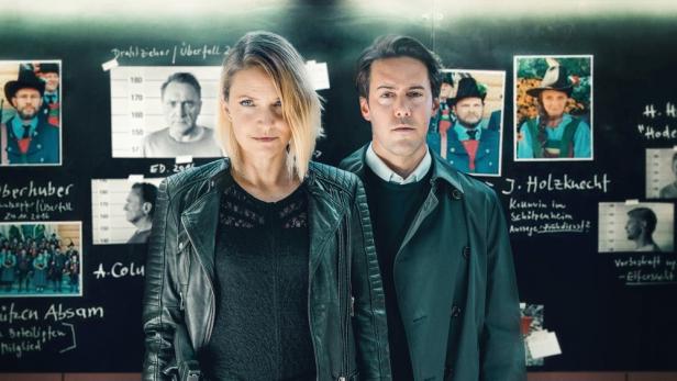 Zwei Ermittler stehen vor einer Tafel mit Fotos und Notizen im Fall „Tote Schlucht“.