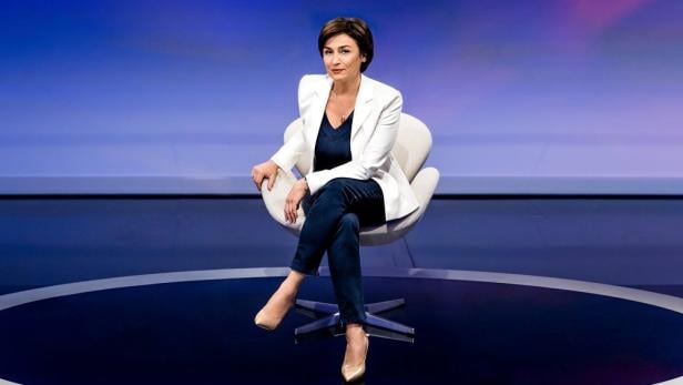 Sandra Maischberger sitzt in einem Sessel vor einem blauen Hintergrund.