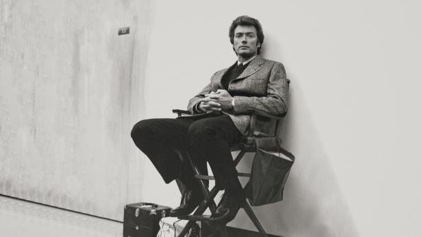 Clint Eastwood sitzt auf einem Regiestuhl in einem Studio.