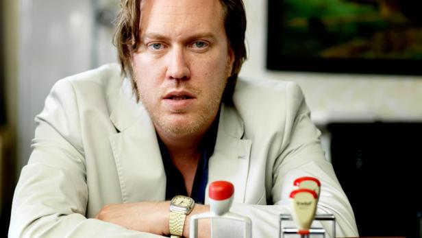 Ein Mann in einem hellen Anzug sitzt an einem Tisch mit zwei Stempeln.