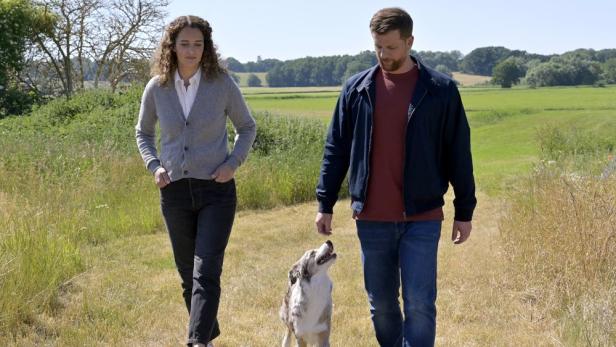 Ein Mann und eine Frau spazieren mit einem Hund durch eine ländliche Gegend.