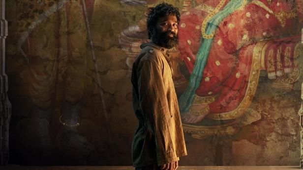 Ein Mann steht vor einem Wandgemälde der hinduistischen Gottheiten Shiva und Lakshmi für den Film „Kubera“.