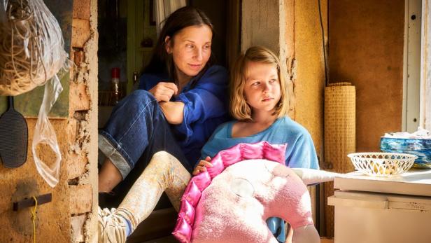 Eine Frau sitzt mit einem Mädchen und einem Einhorn-Kuscheltier in einem Hauseingang.