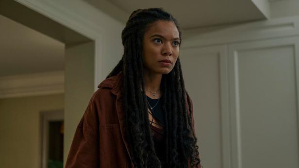 Eine junge Frau mit Dreadlocks und brauner Jacke blickt nachdenklich zur Seite.