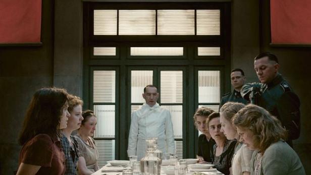 Das Filmplakat zu „Die Vorkosterinnen“ zeigt Frauen, die an einem Tisch sitzen, und einen Koch im Hintergrund.