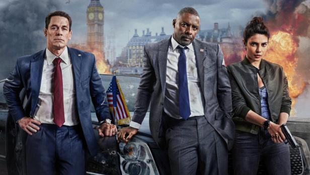 Das Filmplakat für „Heads of State“ zeigt John Cena, Idris Elba und Priyanka Chopra vor einem zerstörten Auto.