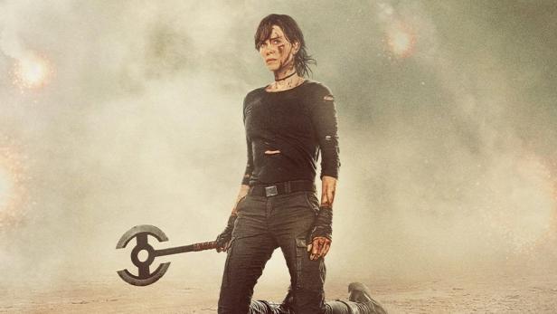 Charlize Theron kniet als Andromache in „The Old Guard 2“ mit einer Axt in der Hand. Im Hintergrund ist ein Hubschrauber zu sehen.