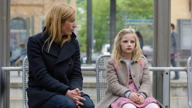 Eine Frau und ein junges Mädchen sitzen an einer Bushaltestelle.