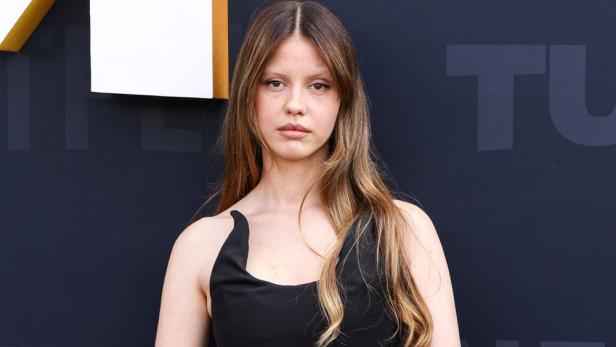 Mia Goth posiert vor einer dunklen Wand.