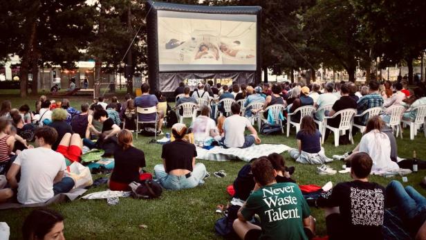 Zuschauer sitzen im Park vor einer Leinwand und schauen einen Science-Fiction-Film.