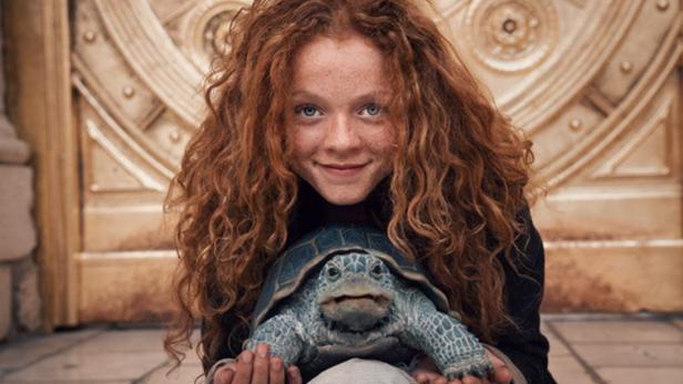 Ein rothaariges Mädchen hält eine Schildkröte im Arm.