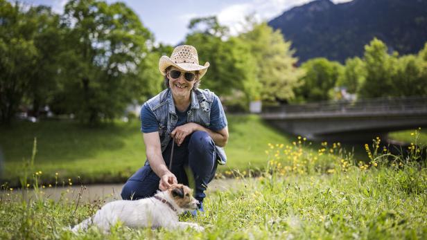 Ein Mann mit Cowboyhut streichelt seinen Hund auf einer Wiese.