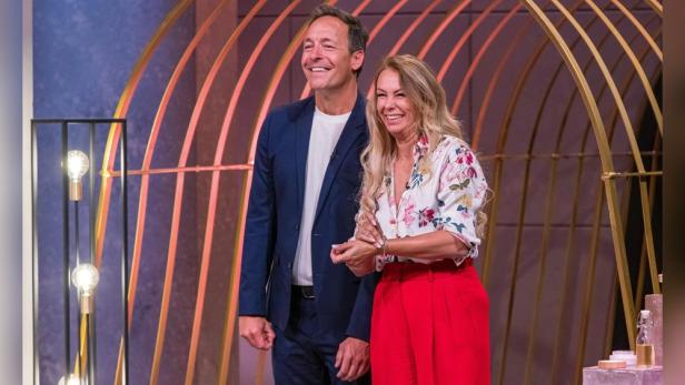 Zwei Personen stehen vor einem goldenen, bogenförmigen Hintergrund in „Die Höhle der Löwen“.