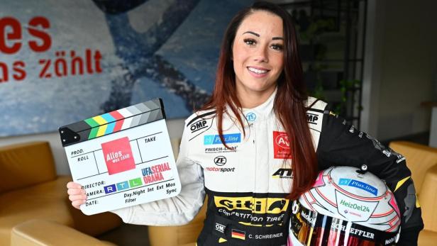 Rennfahrerin Carrie Schreiner hält eine Filmklappe der UFA-Serie „Alles was zählt“.