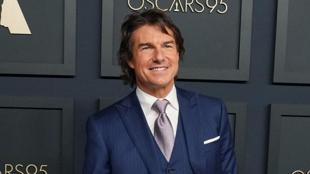 Tom Cruise posiert in einem blauen Anzug vor dem Hintergrund der 95. Oscar-Verleihung.