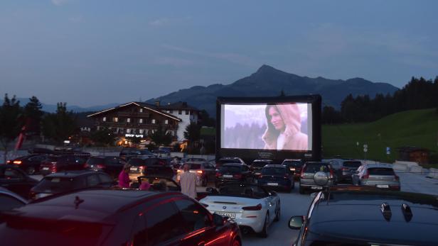 Ein Autokino vor einer Bergkulisse zeigt eine Frau auf der Leinwand.
