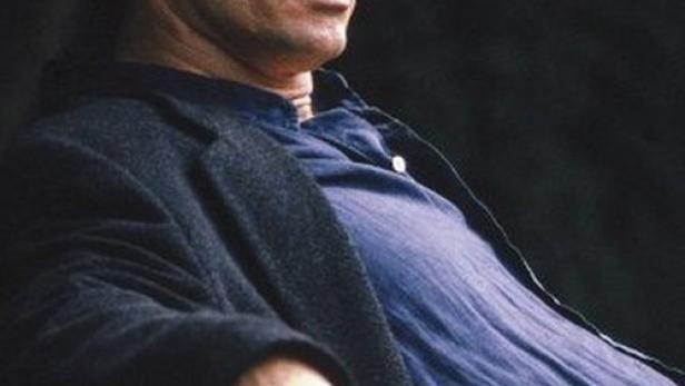 Ein Mann sitzt auf einer Bank, vermutlich eine Szene aus dem Film „Babyraub – Kinder fremder Mächte“.