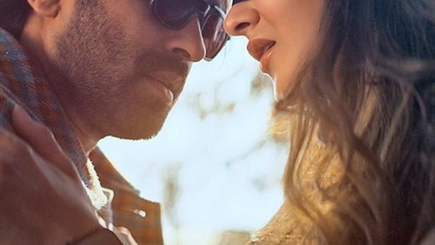 Ein Mann mit Sonnenbrille und eine Frau mit Augenbinde stehen einander sehr nah.