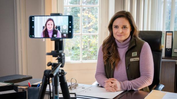 Dr. Mertens sitzt an ihrem Schreibtisch, während sie per Smartphone gefilmt wird.
