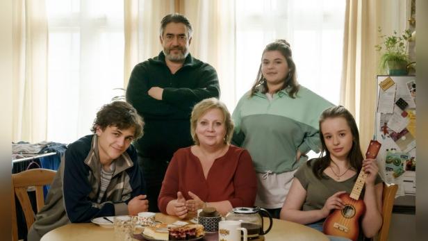 Eine Familie sitzt an einem Tisch mit Kuchen und Getränken.