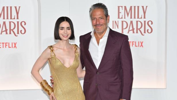 Lily Collins und Darren Star posieren vor einem „Emily in Paris“-Hintergrund.