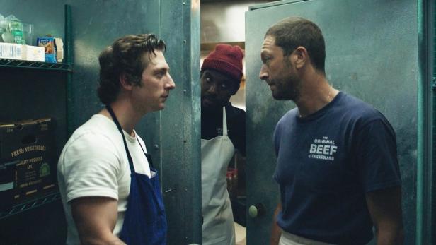 Drei Köche stehen in einem Kühlraum und schauen sich an.