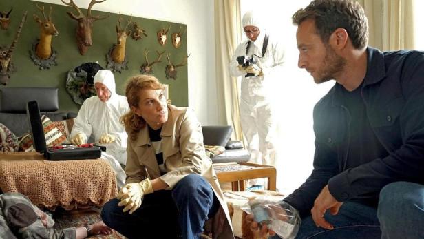 Ermittlerteam am Tatort in einem Wohnzimmer mit Jagdtrophäen an der Wand.
