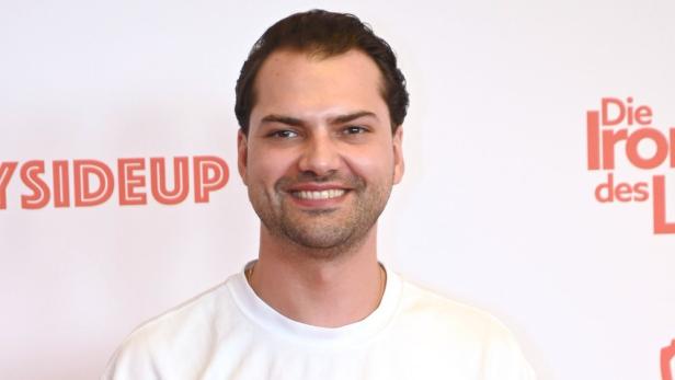 Jimi Blue Ochsenknecht posiert vor Plakaten für „Bayside“ und „Die Irokesen des Lebens“.