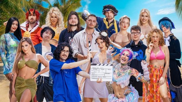 Eine Gruppe von Personen, einige in Kostümen, posiert am Strand mit einer Filmklappe.