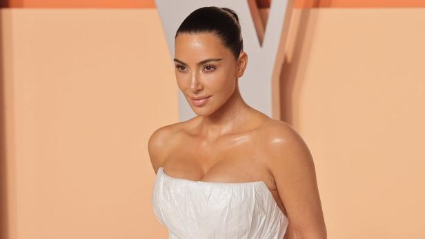 Kim Kardashian in einem weißen, trägerlosen Kleid vor einem hellen Hintergrund.
