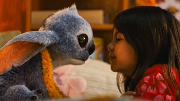 Ein Mädchen schaut einen Plüsch-Stitch mit einer Blumenkette an.