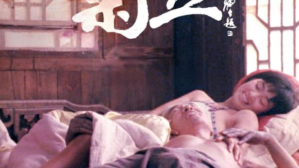 Ein Paar liegt in einem Bett mit roter Blumendecke.