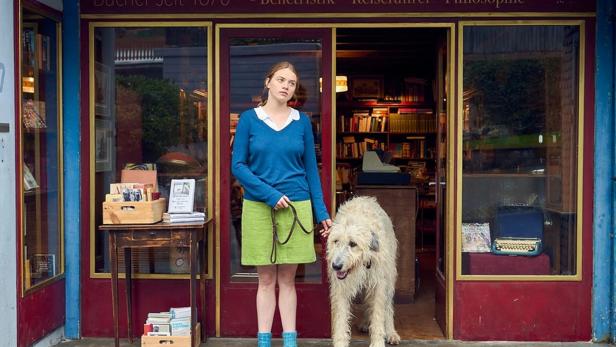 Eine junge Frau steht mit einem Hund vor einem kleinen Buchladen.
