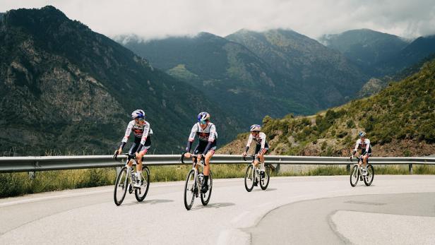 Vier Radfahrer fahren auf einer kurvenreichen Straße in den Bergen.