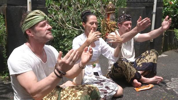 Drei Personen in traditioneller Kleidung sitzen und praktizieren spirituelle Übungen.