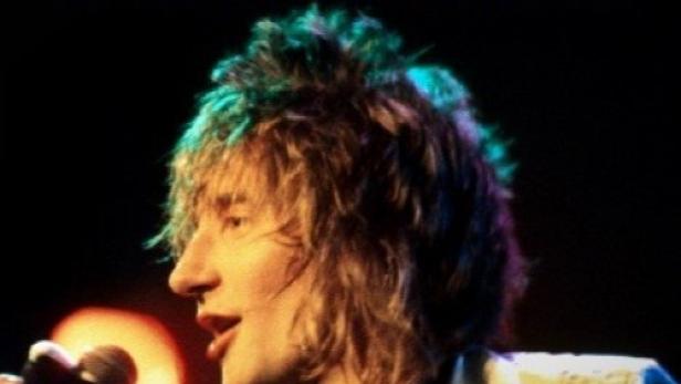 Rod Stewart singt in einem weißen Anzug mit Krawatte in ein Mikrofon.