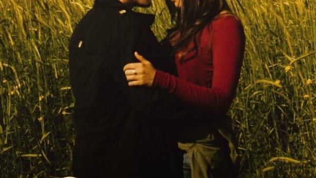 Ein Paar umarmt sich vor einer ländlichen Kulisse, möglicherweise ein Filmposter für „Anduni: Fremde Heimat“.