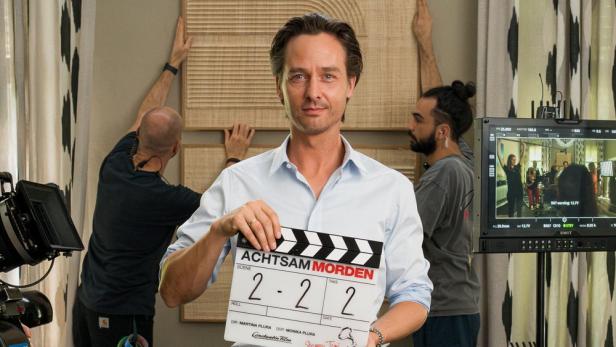 Tom Schilling hält eine Filmklappe für „Achtsam Morden“ in die Kamera.