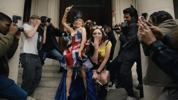 Zwei Frauen posieren in auffälligen Outfits für eine Gruppe von Fotografen.