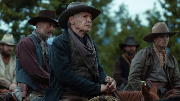 Harrison Ford und andere Schauspieler in Cowboykleidung auf Pferden am Set von „1923“.