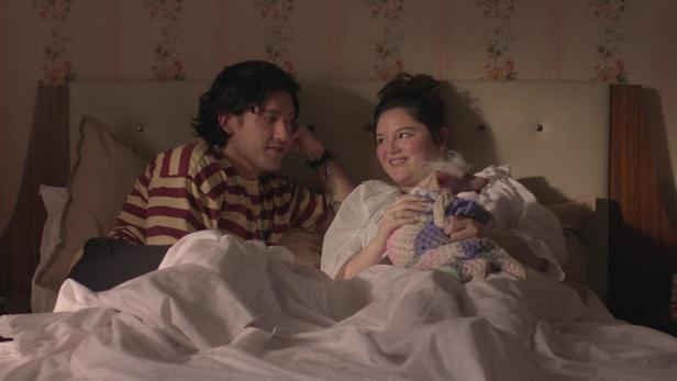 Ein Paar liegt mit einem kleinen Hund im Bett.